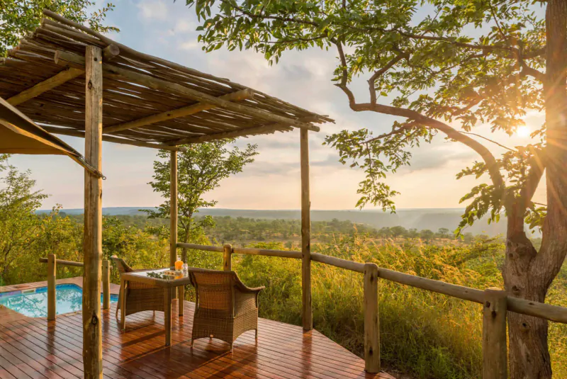 Luxury deck at Old Drift Lodge with hot tub, chairs, table, overlooking lush savanna at sunset.