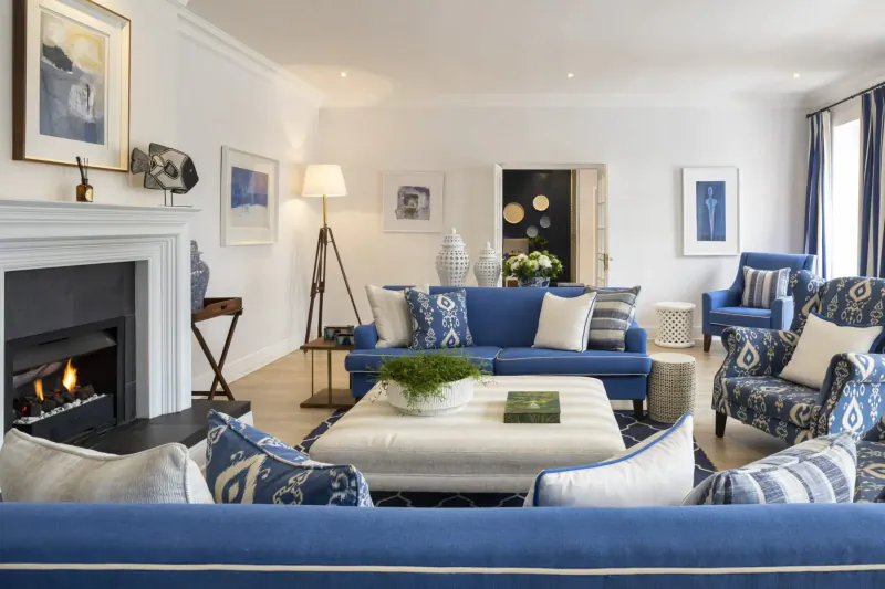 Elegant living room at The Plettenberg Boutique Hotel with blue upholstered furniture, lit fireplace, and art.