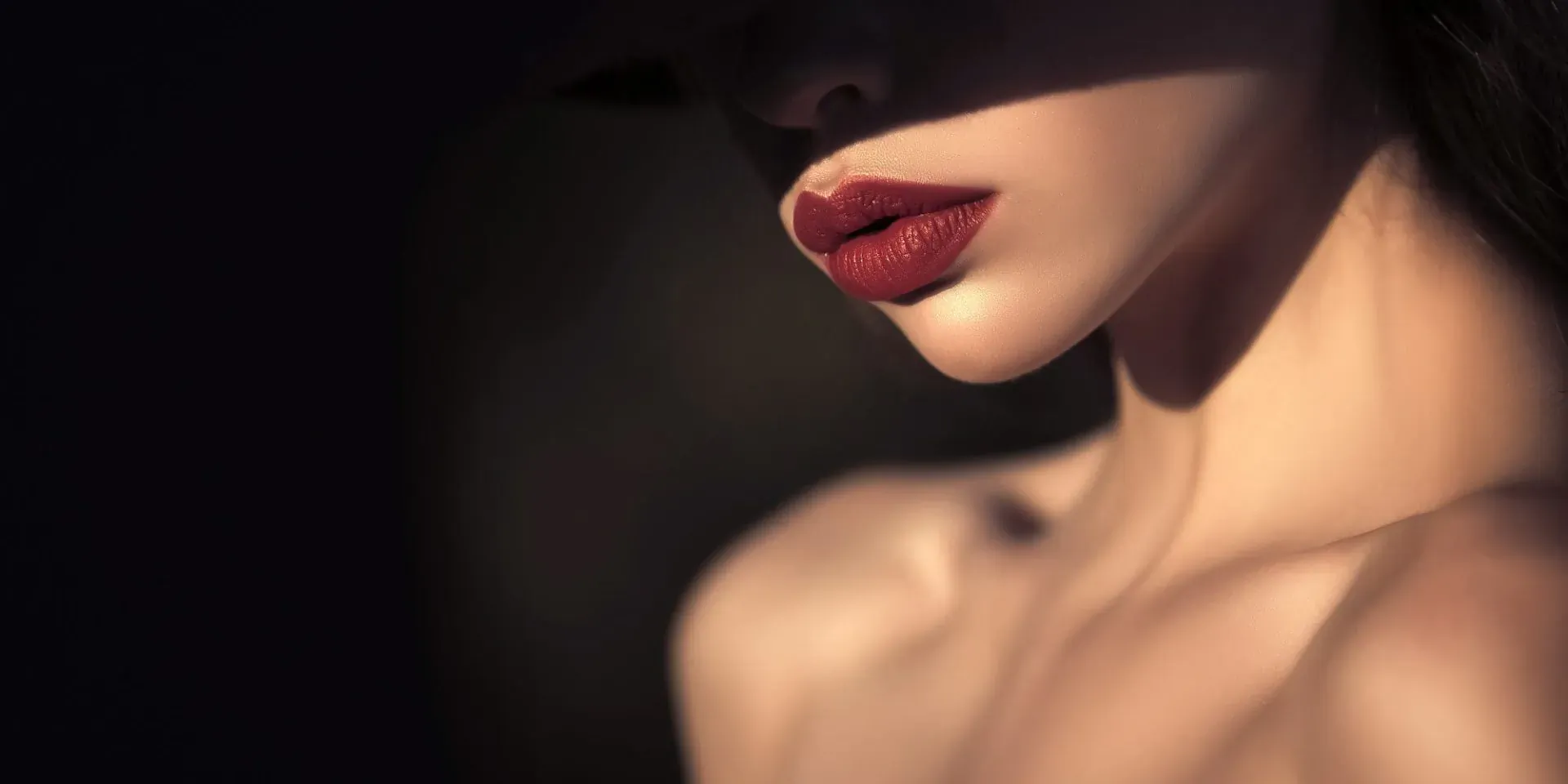 Close-up of woman's face and bare shoulder in dramatic shadow, bold red lips, Mallucci London aesthetics by Dr Jana.
