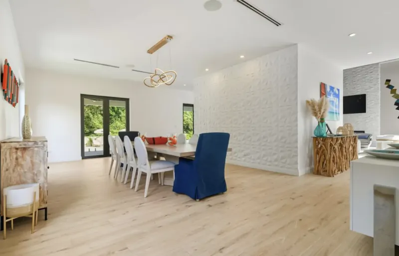 Modern dining room in Lyford Cay luxury home with white oak table, blue chair, white chairs, art, plants, and garden doors.