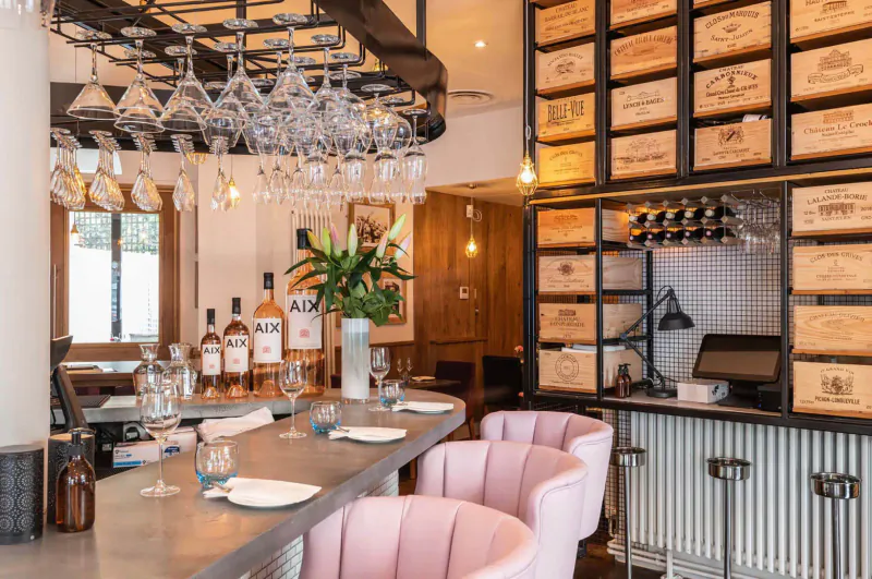 28°-50° Chelsea wine bar interior: pink chairs at concrete bar, AIX rosé bottles, wine glass racks, wood crate walls