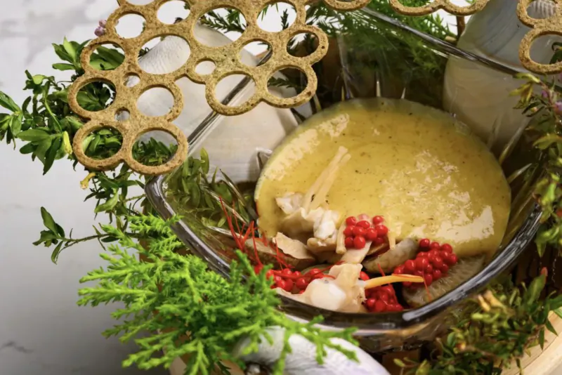 Foraged dish in glass bowl: yellow custard, mushrooms, red berries, greens, gold lattice garnish
