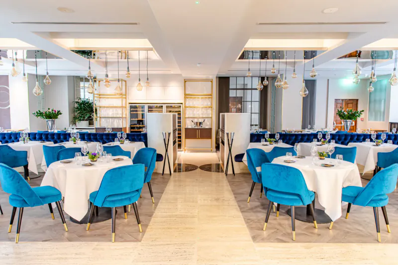 Elegant CORD by Le Cordon Bleu dining gallery with turquoise velvet chairs, white tables, pendant lights, and wine cabinets.