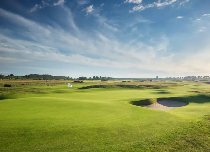 Carnoustie Golf Links: scenic 18th hole bunker with white flag on lush green fairway under partly cloudy sky