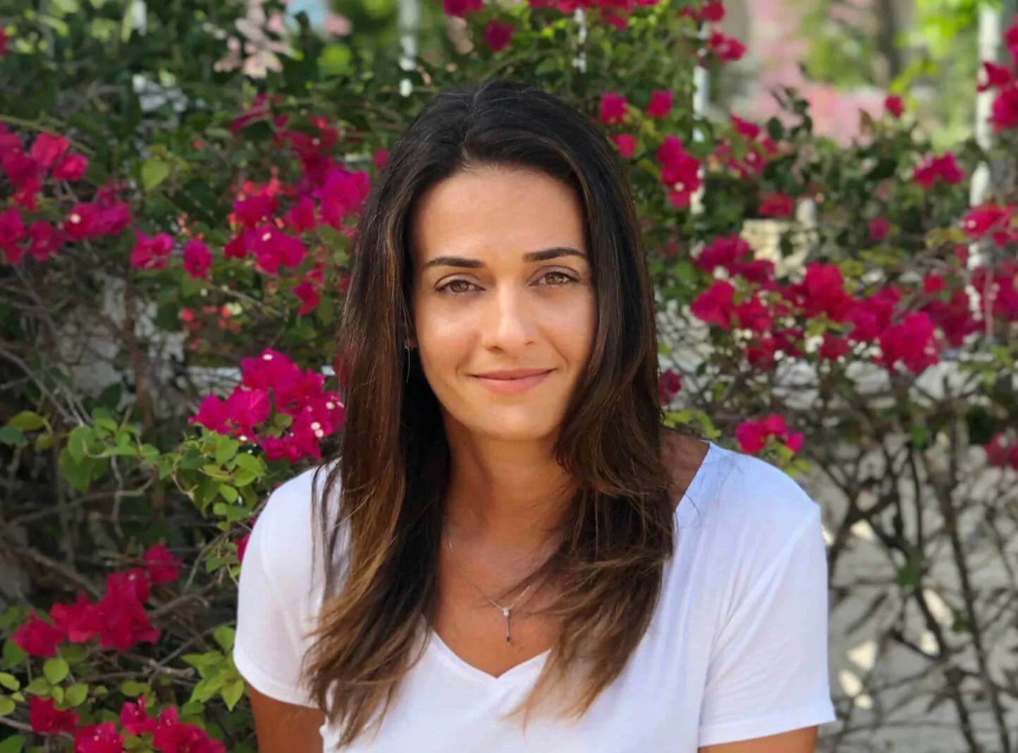 Abire Mansoor, licensed agent, smiling in white top amid vibrant pink bougainvillea