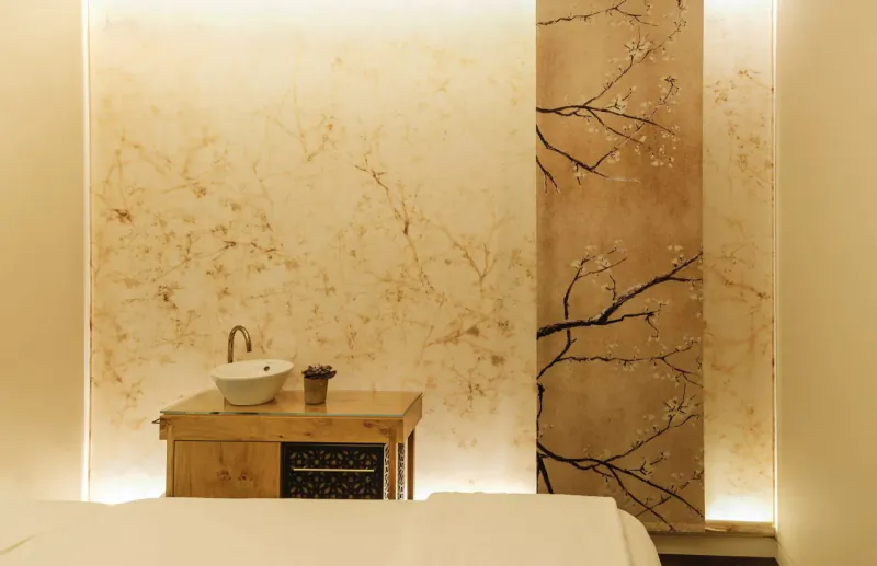 Elegant spa bathroom with wooden vanity, white sink, gold faucet, and cherry blossom wall art.
