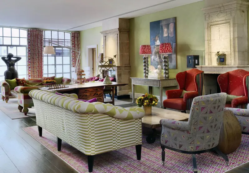 Chic Soho Hotel London living room with green striped sofas, red armchairs, lamps, art, and large windows