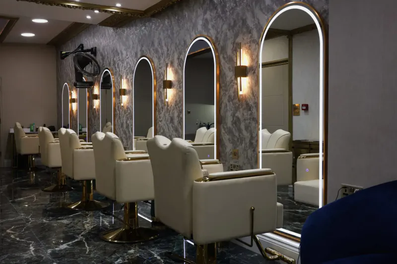 Elegant empty hair salon with white leather barber chairs, arched gold-framed mirrors, and marble floor at The Cut Above.