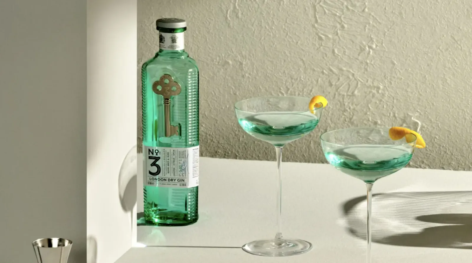 No.3 Gin bottle with gold key logo next to two green Dry Martinis garnished with lemon twists on a table