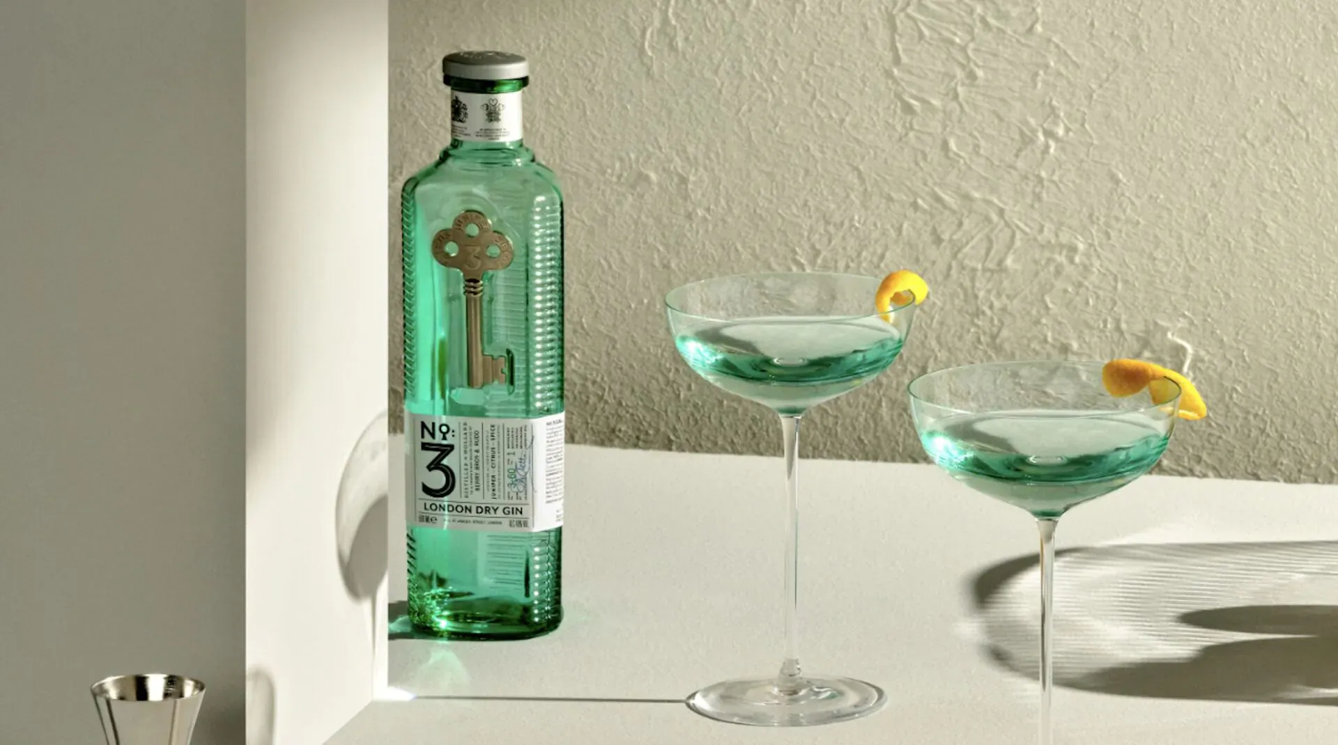 No.3 Gin bottle with gold key logo next to two green Dry Martinis garnished with lemon twists on a table