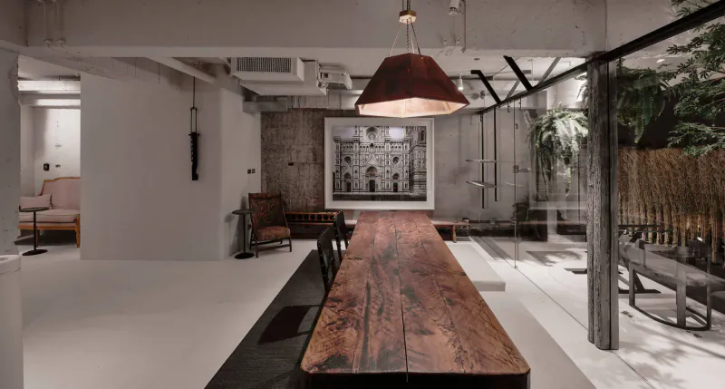 Stylish contemporary restaurant interior with long wooden dining table, chairs, pendant light, exposed beams, and indoor plants.