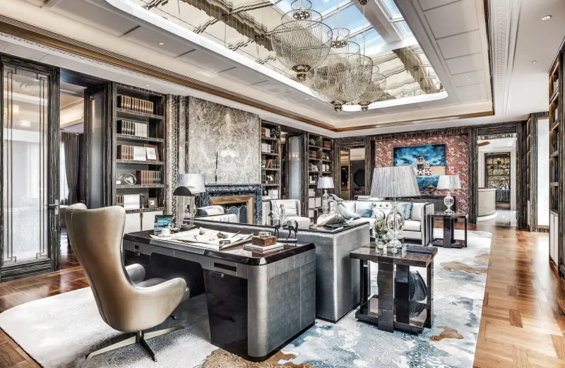 Luxurious modern office with skylight, gray swivel desk, bookshelves, lamps, and abstract art.