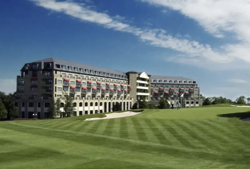 Celtic Manor Resort hotel with red banners beside manicured golf course under blue sky