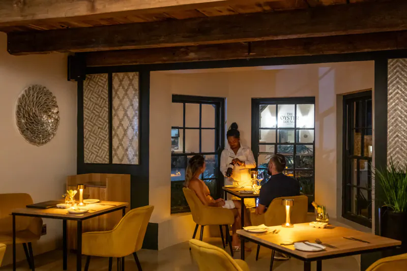 Elegant Oyster Suites lounge at Abalone Hotel: diverse group dining at candlelit wooden table amid warm lighting and windows.