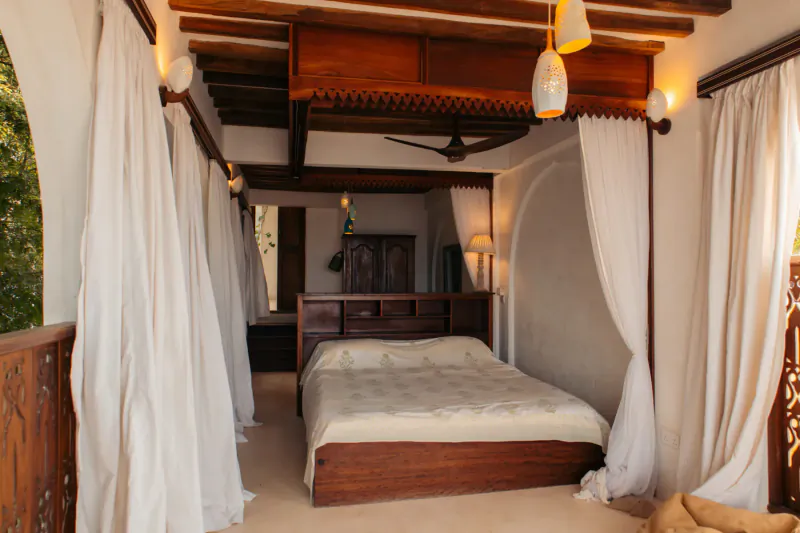 Serene Swahili bedroom at Kijani Hotel Lamu with wooden bed, white curtains, beamed ceiling, and balcony view.