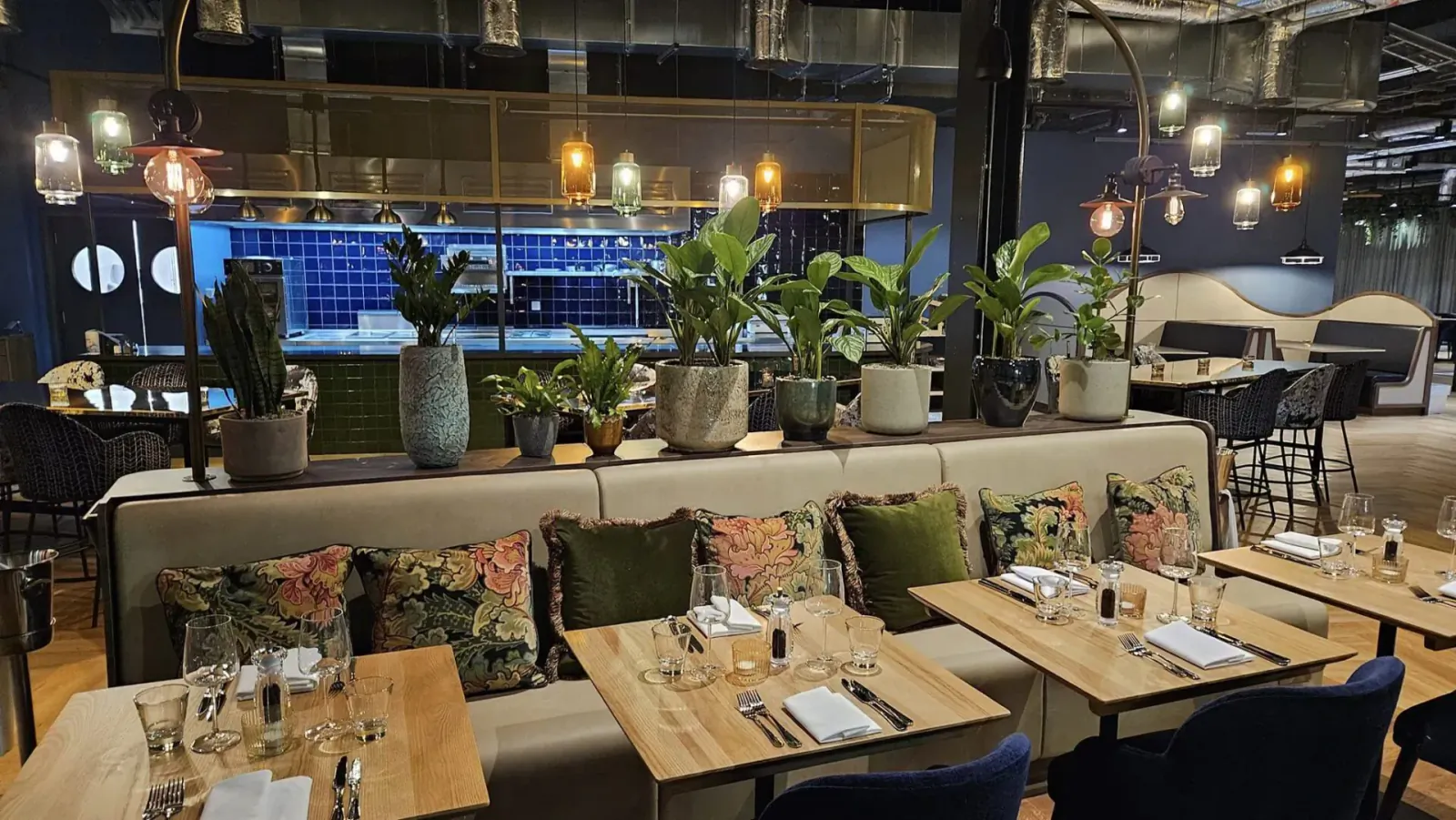 Modern Hotel Indigo lounge with blue tiled bar, potted plants, curved sofas, wooden tables, and pendant lights.