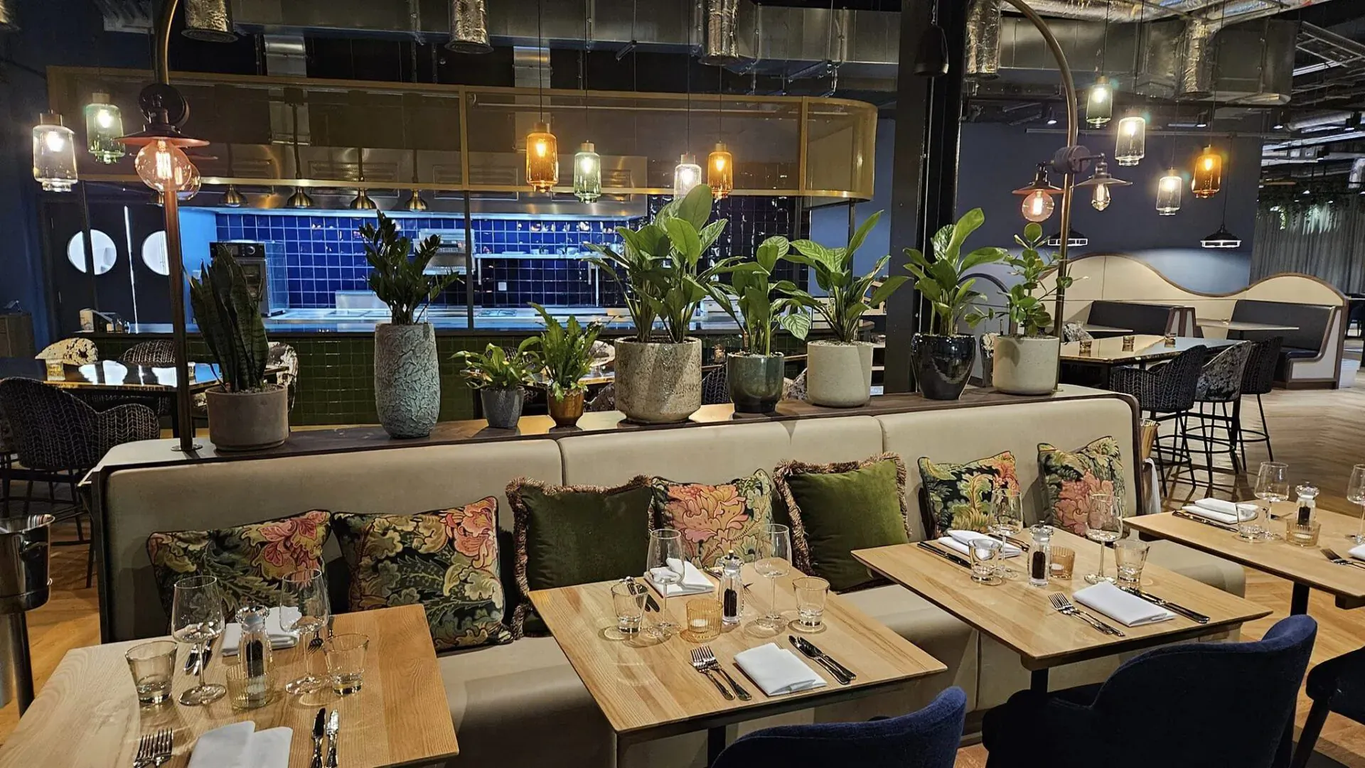 Modern Hotel Indigo lounge with blue tiled bar, potted plants, curved sofas, wooden tables, and pendant lights.