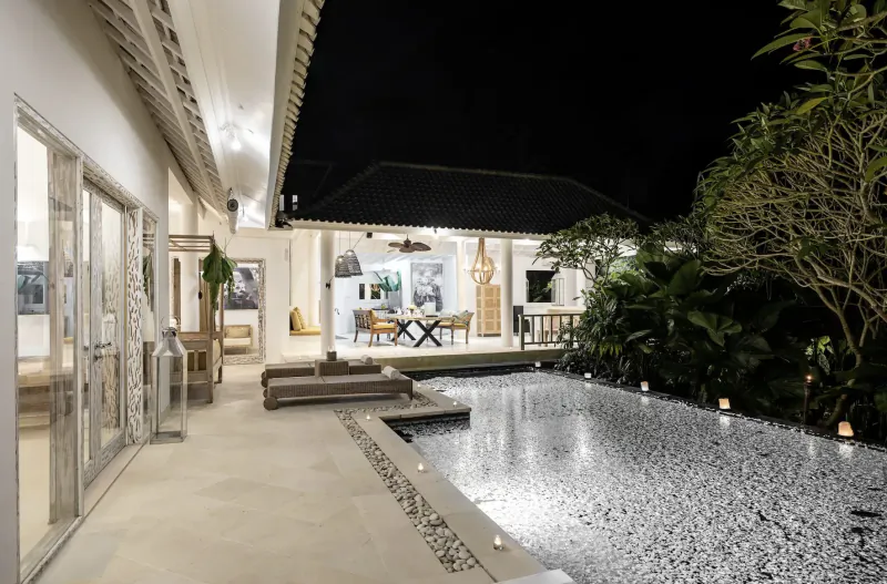 Night view of Sungai Jungle Villas in Bali: modern white villa with pool, lounge, dining area, and lush tropical plants.