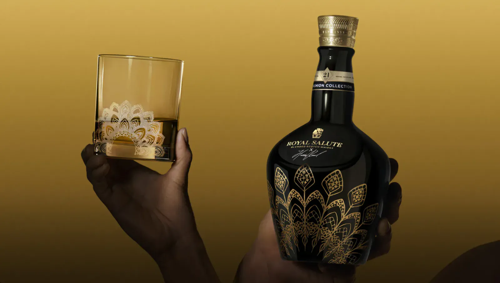 Hands holding Royal Salute whisky bottle with intricate gold peacock design and a glass of whisky on the rocks