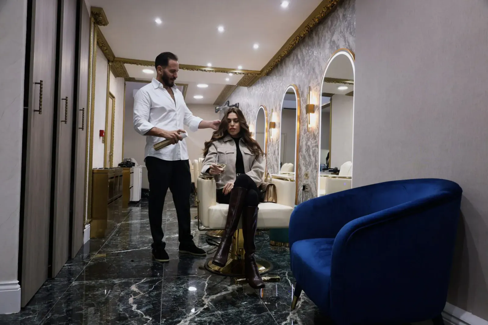 George Vallossian styling a woman's hair in a luxurious salon with arched mirrors and blue chairs
