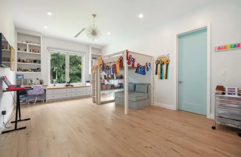 Bright child's bedroom in Lyford Cay home with loft bed draped in colorful ribbons, bookshelves, desk, and turquoise door.