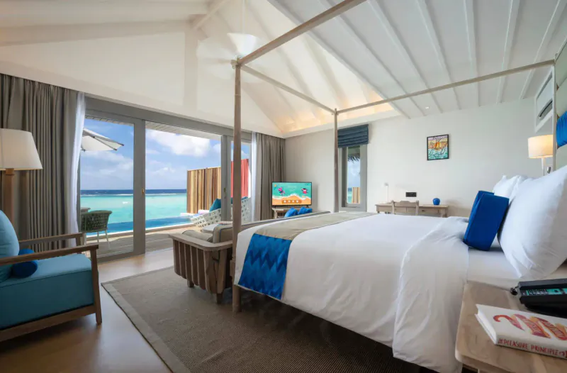 Luxurious Cora Cora Maldives overwater villa bedroom with king bed, ocean view, and turquoise accents.