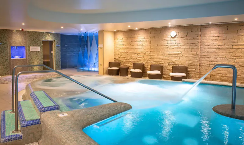 Luxurious indoor pool with glowing blue water, steps, chrome rails, lounge chairs, and brick walls at a romantic retreat.