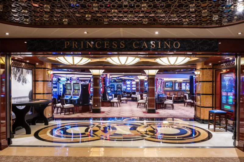 Grand entrance to Princess Casino onboard cruise ship, with slot machines, chandeliers, and ornate floor.