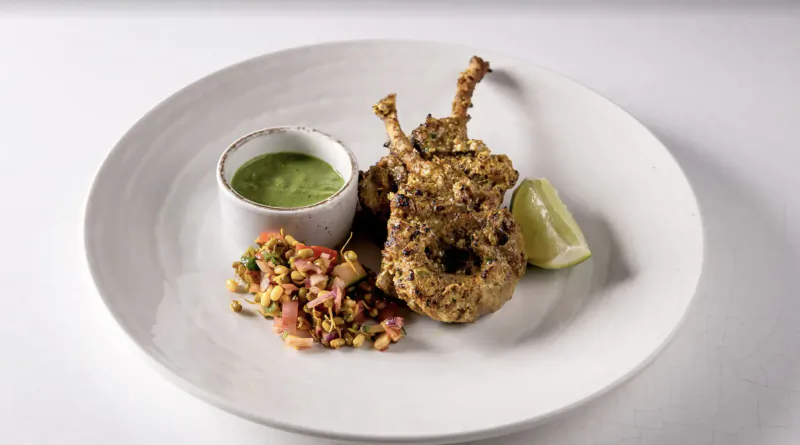 White plate with herb-crusted chicken lollipops, green sauce dip, tomato salsa, and lime wedge