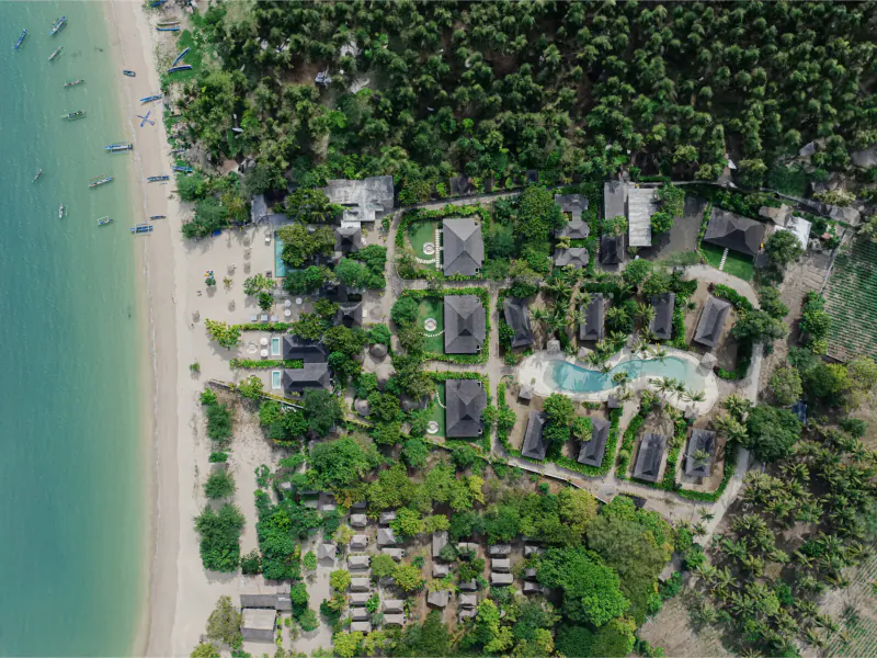 Aerial view of Kuara Lombok boutique resort with thatched villas, infinity pool, lush gardens, and beachfront on turquoise sea.
