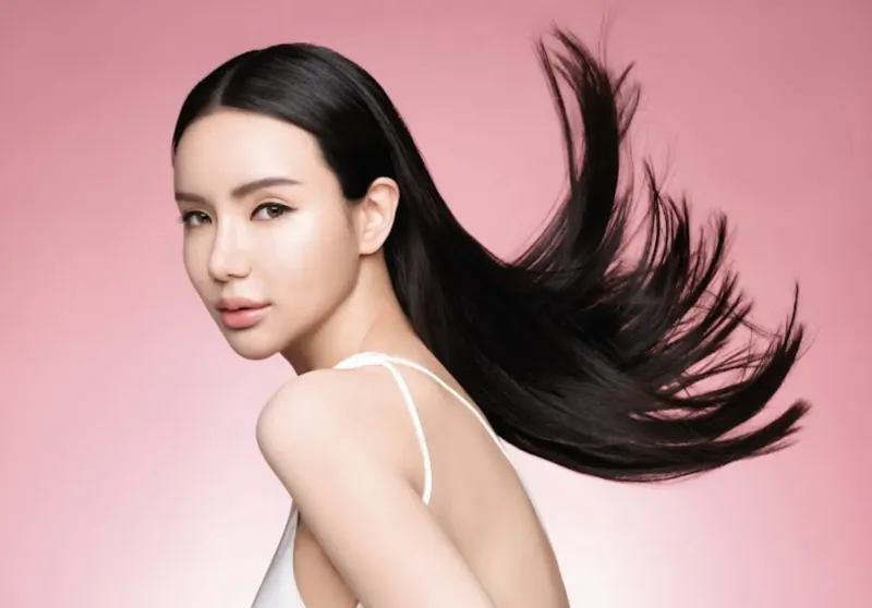Asian woman with long flowing black hair, profile view in white camisole against pink background