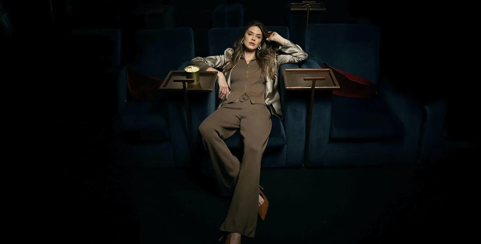 Woman in brown lounge suit reclining relaxed in dark cinema theater seats with tray tables