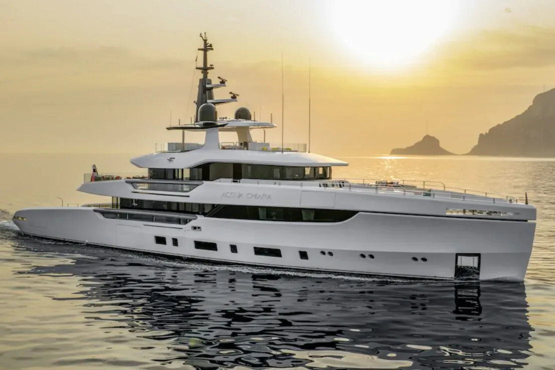 White 47m superyacht Acqua Chiara by Hot Lab cruising at sunset near rocky cliffs