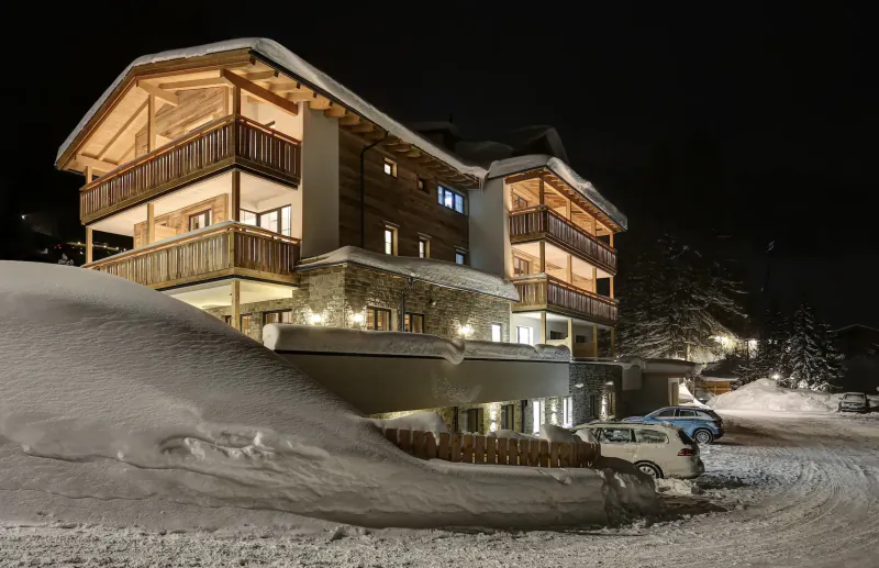 Hotel Kösslerhof in St Anton am Arlberg at night: luxury chalet with wooden balconies, snow-covered grounds, parked cars, lit warmly.