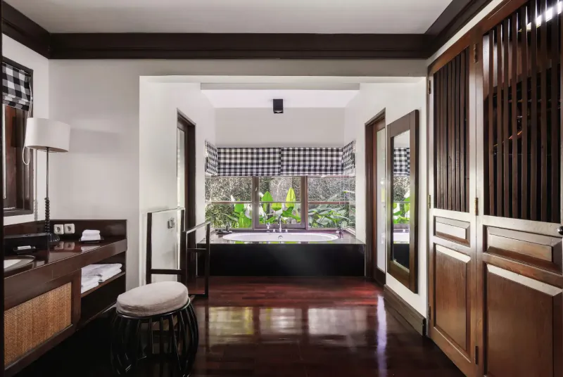 Luxurious Kayumanis Ubud Bali hotel bathroom with deep black bathtub, tropical garden view, dark wood floors and accents.
