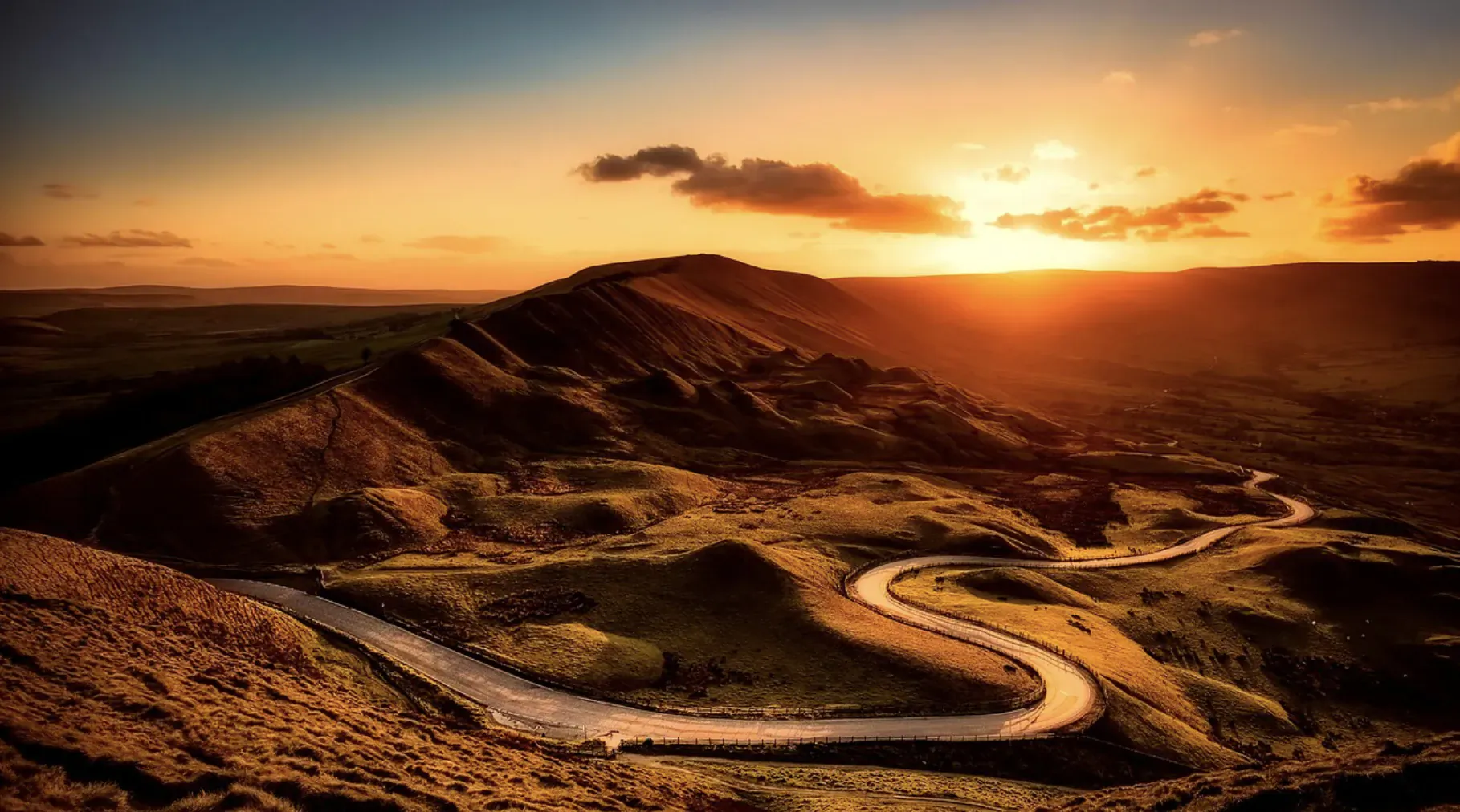 Winding road snakes through rugged UK hills at golden sunset during road trip