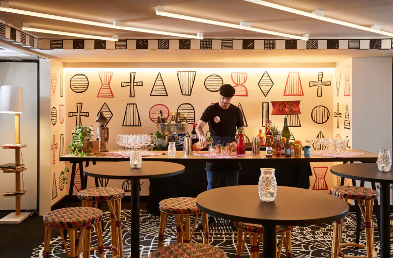 Bartender mixing drinks at modern Mama Shelter bar in East London, geometric wall art, stools, glassware.
