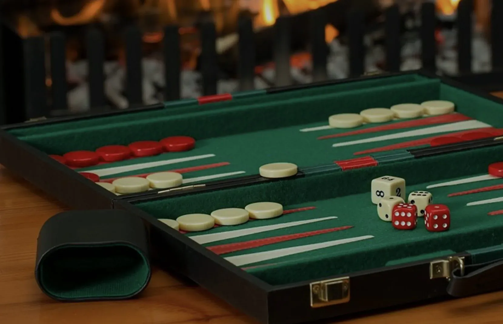 Backgammon board with red and white checkers, dice, in green felt case by cozy fireplace.