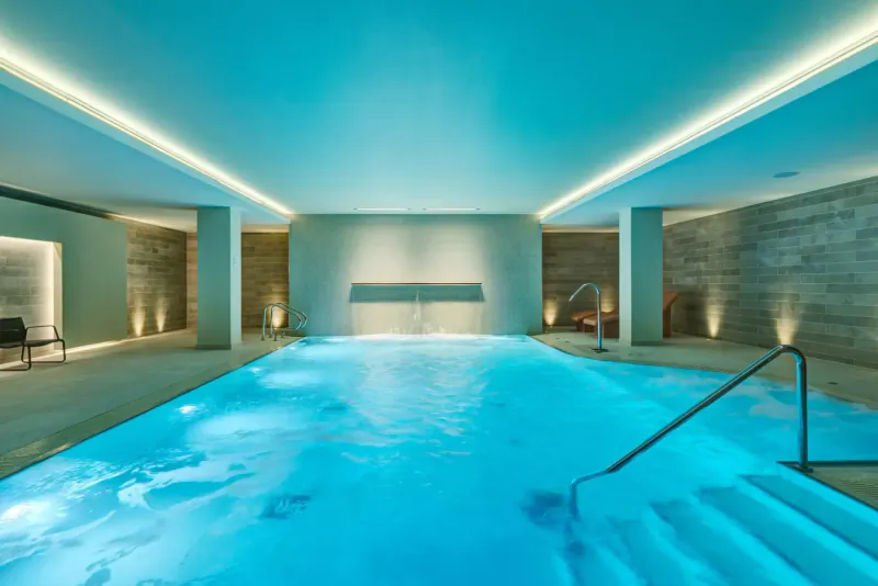 Elegant indoor pool at Apex City of Bath Hotel with blue-lit water, stone walls, columns, and lounge chairs.