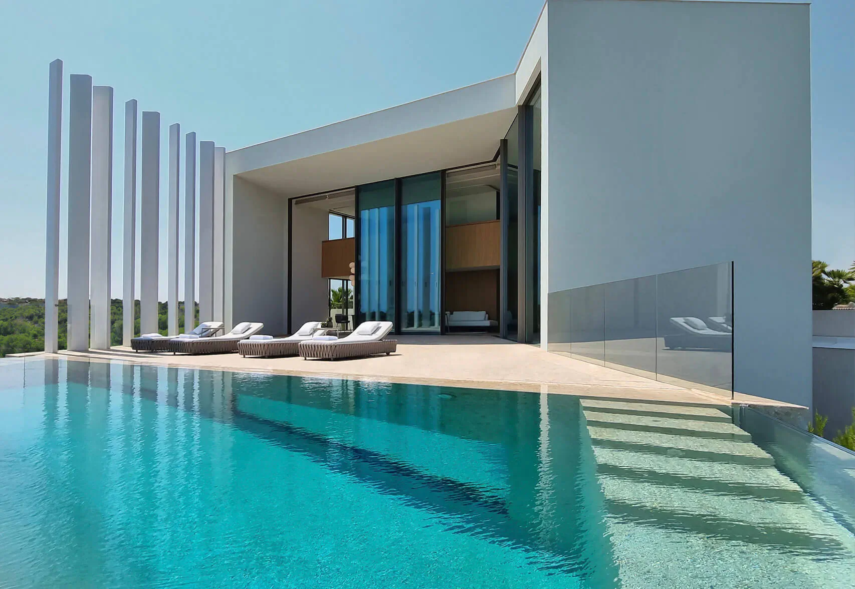 Modern white Villa Armani with infinity pool, loungers, glass walls, and columns on Costa Blanca hillside