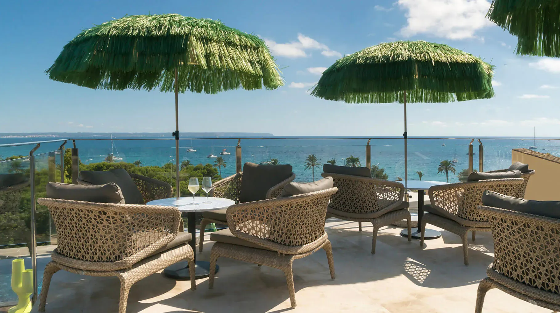 Rooftop lounge at El Llorenç Parc de la Mar with green fringed umbrellas, wicker chairs, tables with wine glasses, and sea view.