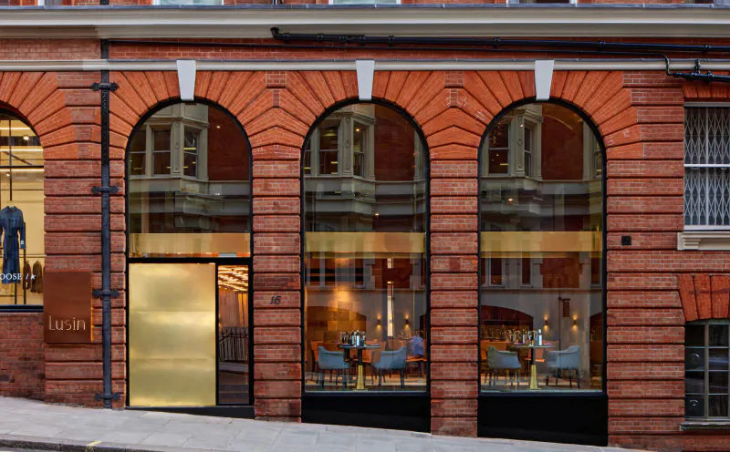 Lusin Mayfair gallery facade: red brick arches, gold entrance, mannequins in window, chairs inside.