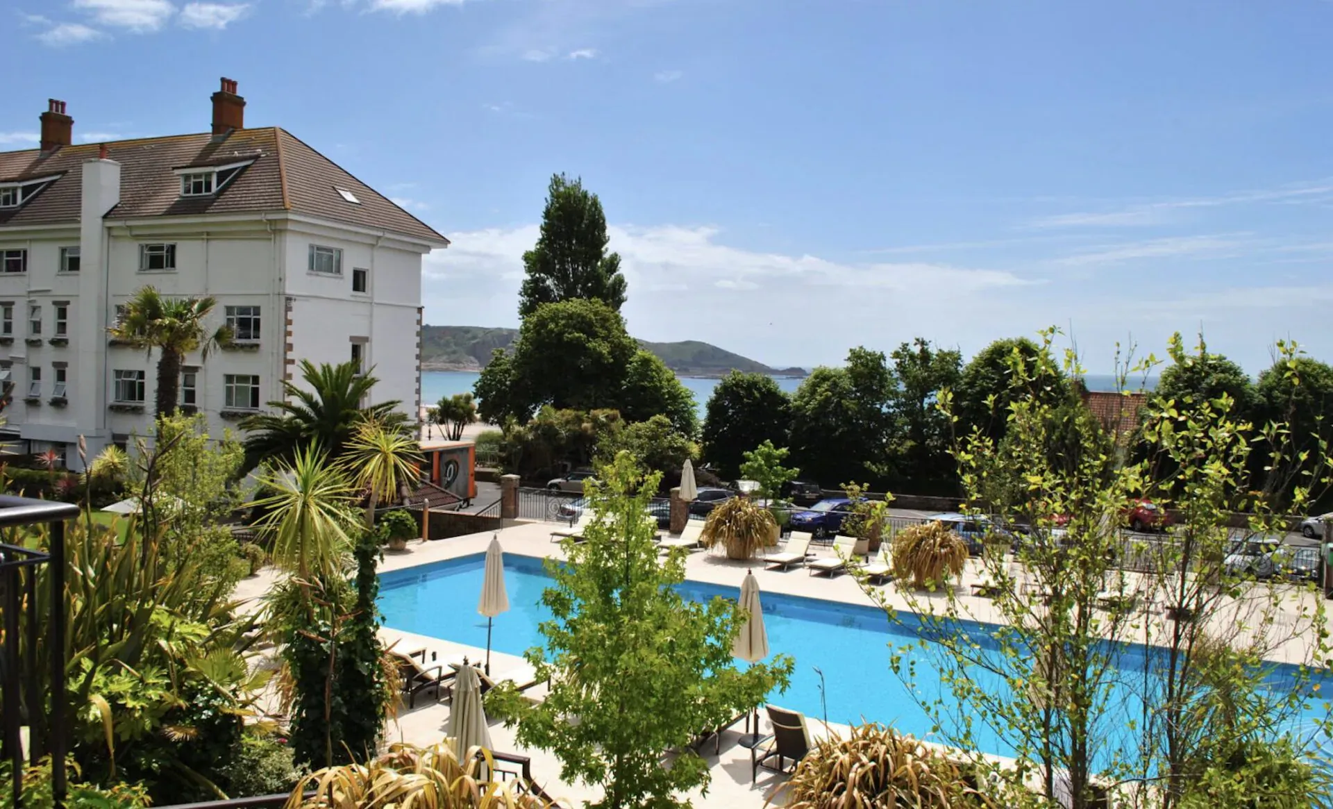 St. Brelade’s Bay Hotel in Jersey: lush gardens, blue pool with umbrellas and loungers, bay view under clear skies