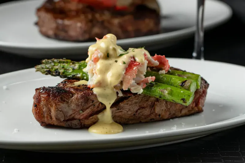 Grilled steak topped with hollandaise, crab, and asparagus on white plate at STK restaurant