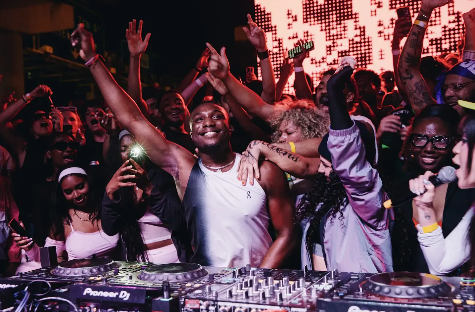 DJ at Pioneer decks with energetic crowd dancing, arms raised, at Clubhouse Nights Miami Boiler Room debut.