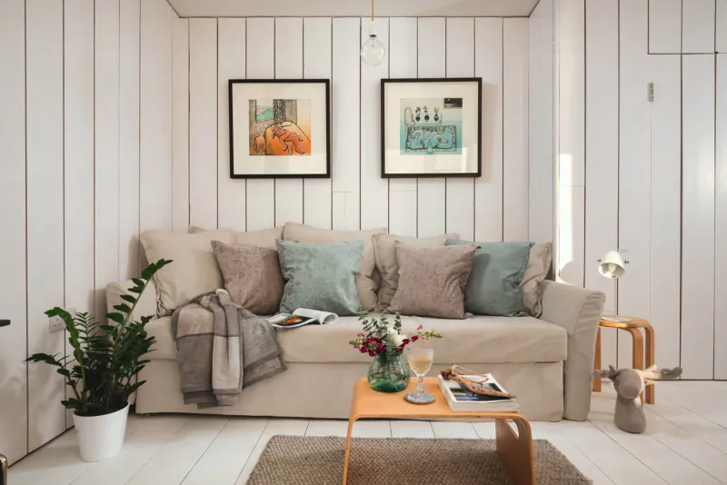 Cozy living room in Boutique Retreats stay with beige sofa, plants, flowers, books, and modern art on white paneled walls.
