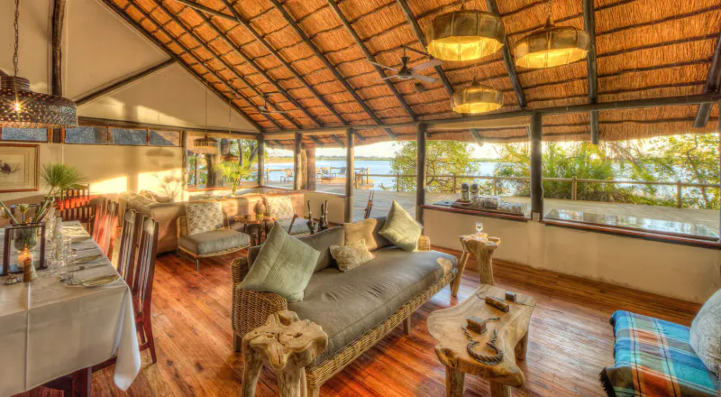 Spacious thatched Xugana Island Lodge interior with plush sofas, wooden tables, dining setup, and lake views.