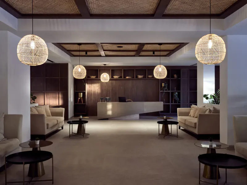 Contessina Hotel Zakynthos lobby with woven pendant lights, wooden wall, white reception desk, beige sofas, and tables.