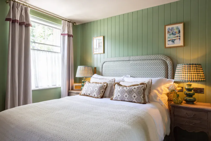 Cozy green-paneled bedroom with white upholstered bed, pillows, lamps, and window drapes in The George & Dragon Marlow.