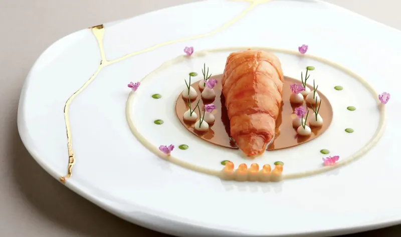 Saint Pierre dish: whole cooked langoustine on white plate with gold kintsugi, purple flowers, microgreens, and sauce dots.